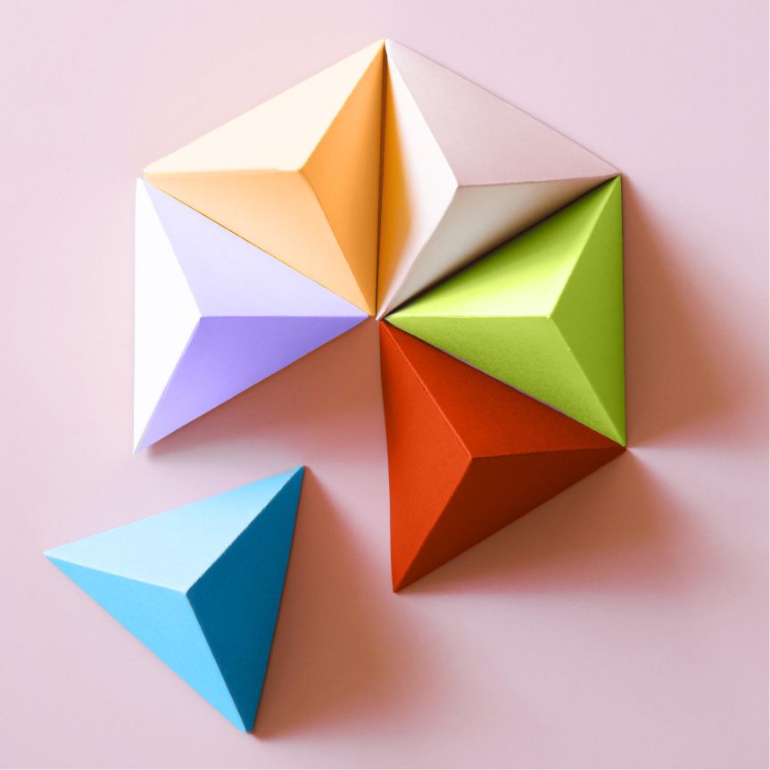 Origami paper triangles in various colors arranged on a soft pink background, symbolizing creativity and artistic expression.

